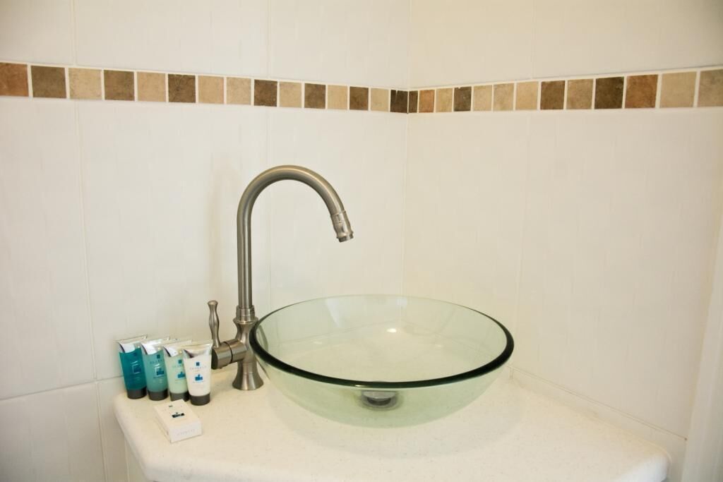 A bathroom with a glass bowl sink, a modern faucet, and toiletries on the counter.