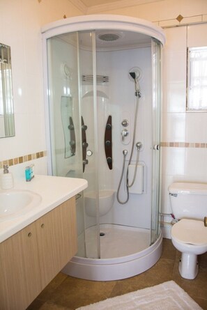 A modern bathroom with a glass-enclosed shower, a white toilet, and a vanity with a mirror. - Morne SeaView Apartments (Castries)