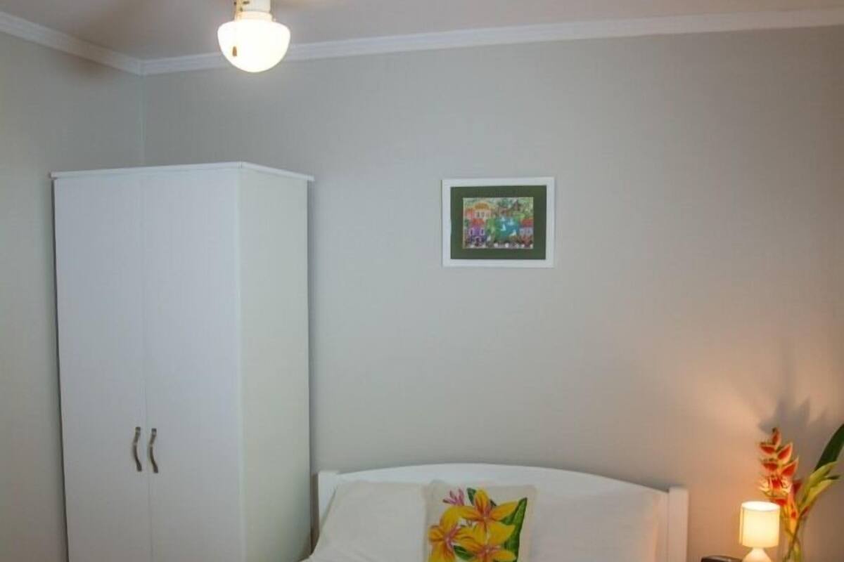 A bedroom with a bed, a nightstand with a lamp, a ceiling fan, and a wardrobe.