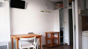 A small, open-plan room with a wooden table and chairs, a TV mounted on the wall, and a door leading to a closet.