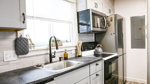 A modern kitchen with a black countertop, stainless steel appliances, and white cabinetry. - Whispering Pines by Cottonwood Lodging (Brighton)