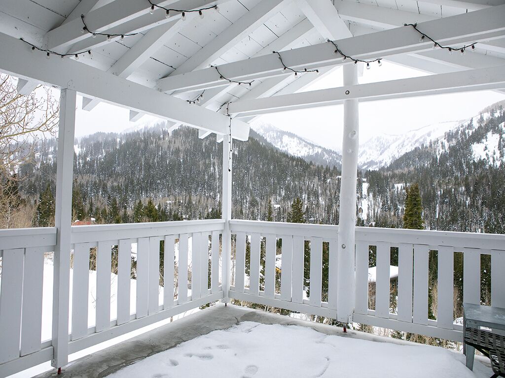 A covered outdoor area with a white railing, snow on the ground, and a view of snow-covered mountains.