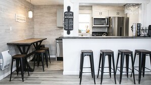 A modern kitchen with a wooden island, bar stools, and a welcome sign. - Whispering Pines by Cottonwood Lodging (Brighton)