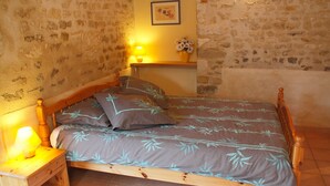 A bedroom with a wooden bed, a nightstand with a lamp, a small shelf with a vase of flowers, and a picture on the wall. - Hyper-Gite: very large barn converted into gites (Corpe)