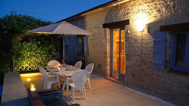 An outdoor patio with a table and chairs, a brick barbecue, and a wall with a door and window. - Hyper-Gite: very large barn converted into gites (Corpe)