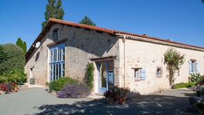 A stone building with a tiled roof, a large window with blue shutters, and potted plants in the foreground. - Hyper-Gite: very large barn converted into gites (Corpe)