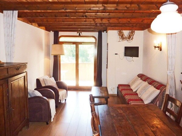 A wooden-floored room with a sofa, chairs, a table, and a TV mounted on the wall.