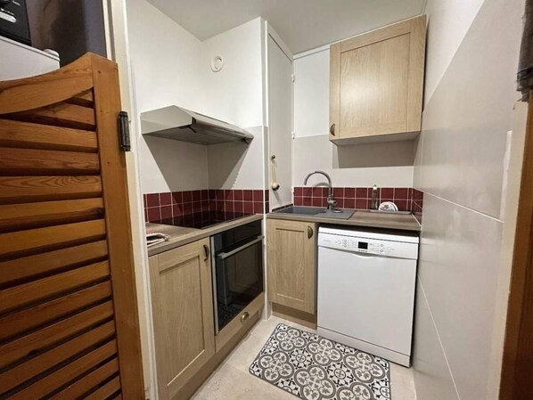 A compact kitchen with wooden cabinets, a built-in oven, a dishwasher, and a tiled backsplash.