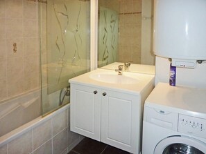 A bathroom with a glass-enclosed shower, a sink, and a washing machine.
