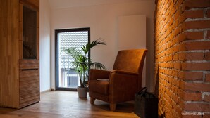 A modern living room with a wooden cabinet, a leather armchair, a potted plant, and a brick wall.