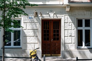 Ein Gebäude mit einer großen Holztür, ein Fahrrad davor und ein Baum zur Linken.