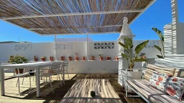 Eine Terrasse im Freien mit Holzboden, weißer Möbel und Topfpflanzen.