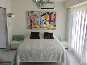 Quarto com cama, mesa de cabeceira, luminária e um quadro na parede.