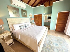 A bedroom with a bed, bedside tables, a nightstand, a mirror, and a door leading to a bathroom.