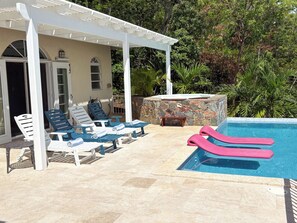 A pool area with lounge chairs, a hot tub, and a stone wall.