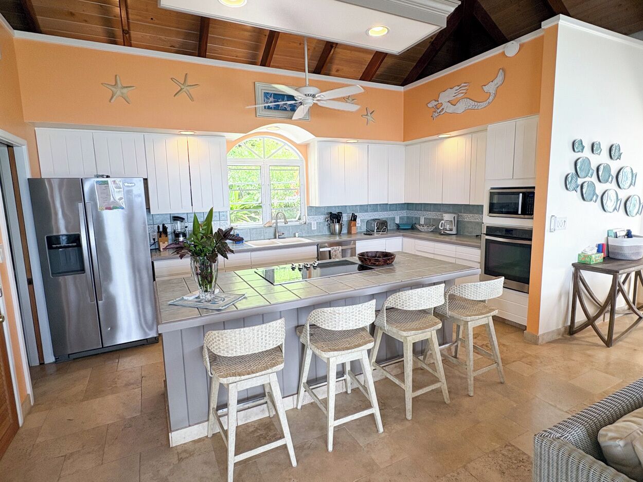 A kitchen with a central island, white cabinetry, a stainless steel refrigerator, and a ceiling fan.