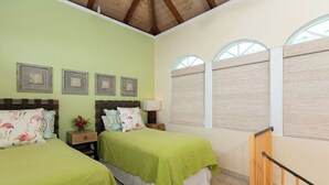 A room with two beds, each with a green bedspread and floral pillows, wooden headboards, and a nightstand with a lamp.