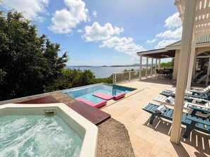 A pool area with a hot tub, lounge chairs, and a view of the sea.