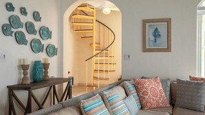 A living room with a curved staircase, a sofa with patterned cushions, and wall-mounted fish decorations.