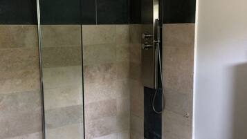 Een douche met glazen wanden, een handdouche, betegelde wanden en een zwarte vloer.
