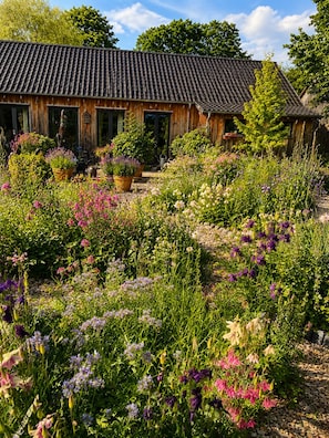 Una casa de madera con techo de tejas rodeada de un jardín con diversas flores.