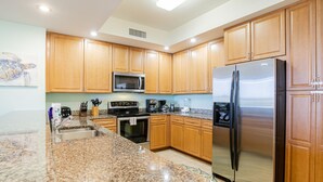 Una cocina con encimeras de granito, armarios de madera, electrodomésticos de acero inoxidable, incluyendo un refrigerador y un microondas, y salpicadero de azulejos.