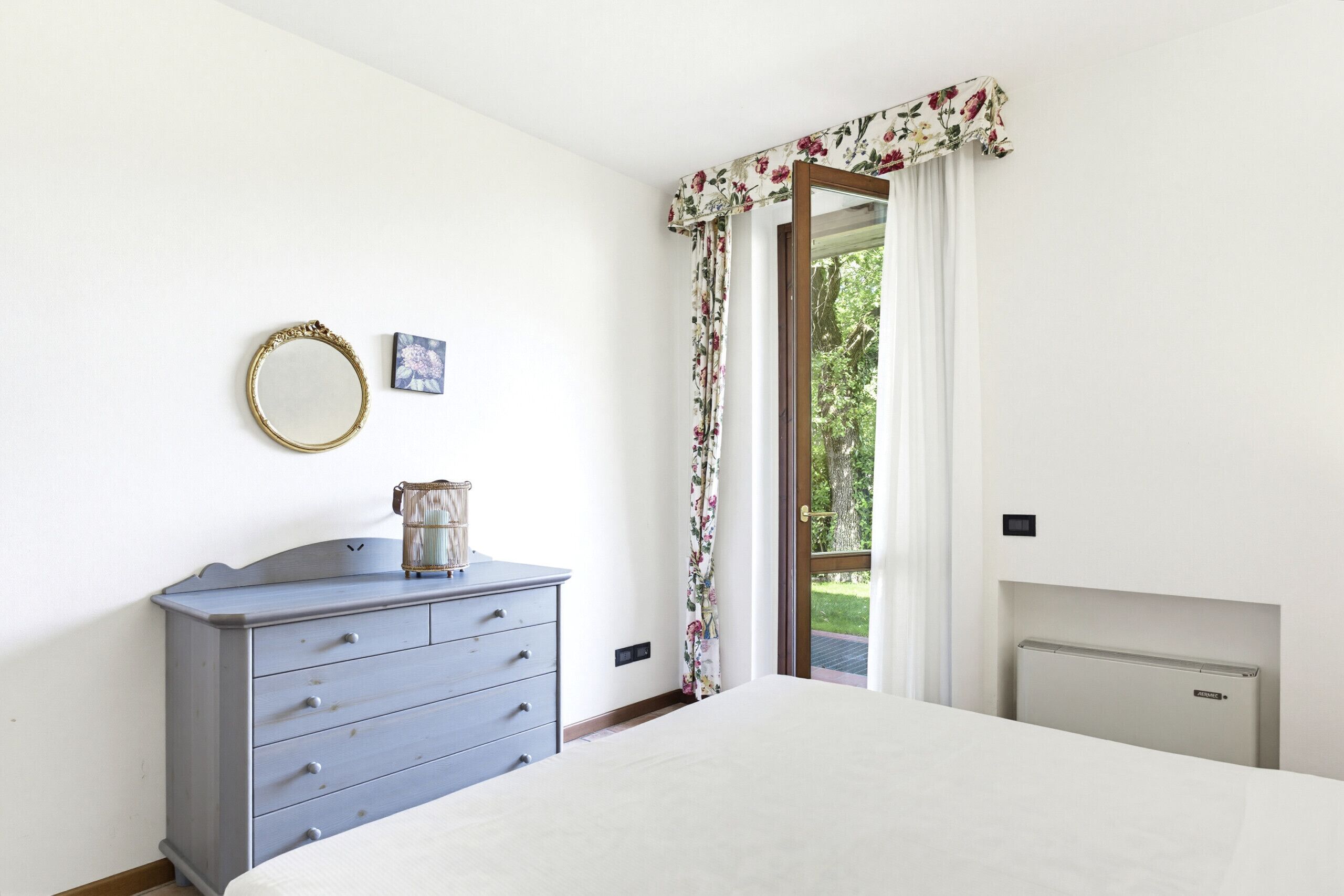 A bedroom with a bed, dresser, mirror, and a view through a door.