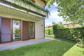 Une maison moderne dotée d’une grande porte vitrée, d’un petit jardin et d’un balcon en bois.