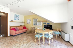 Un'accogliente zona giorno con divano, tavolo da pranzo, sedie, televisore e termosifone.