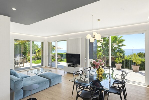 A modern living room with a sofa, a glass dining table, and a TV.
