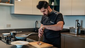 A modern kitchen with a stove, pots, a cutting board, and a person cooking. - Regarda - Luxury "Villa Orizzonti" with private pool and breathtaking lake view (Bardolino)