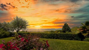 A garden with a view of the sunset over a body of water, featuring well-maintained grass and various plants. - Regarda - Luxury "Villa Orizzonti" with private pool and breathtaking lake view (Bardolino)