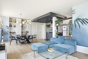 A modern living room with a blue sofa, a glass coffee table, and a dining area with a black table and chairs. - Regarda - Luxury "Villa Orizzonti" with private pool and breathtaking lake view (Bardolino)