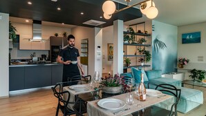 A modern dining area with a table set for two, a kitchen in the background, and a living area with a sofa and decorative plants. - Regarda - Luxury "Villa Orizzonti" with private pool and breathtaking lake view (Bardolino)