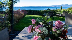 A garden with a table and chairs, a view of the sea, and a clear sky. - Regarda - Luxury "Villa Orizzonti" with private pool and breathtaking lake view (Bardolino)