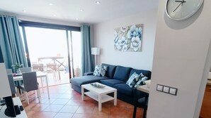 A modern living room with a sofa, coffee table, and a wall clock. - Apartamento Idaira Paradise (Playa Paraíso)