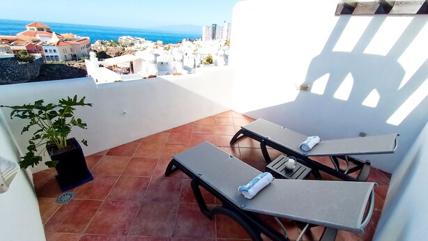 A terrace with two sun loungers, a potted plant, and a view of the sea and buildings. - Apartamento Idaira Paradise (Playa Paraíso)