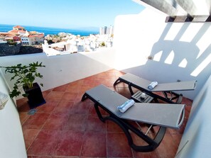 Una terrazza con due lettini, una pianta in vaso e vista sul mare e sugli edifici.