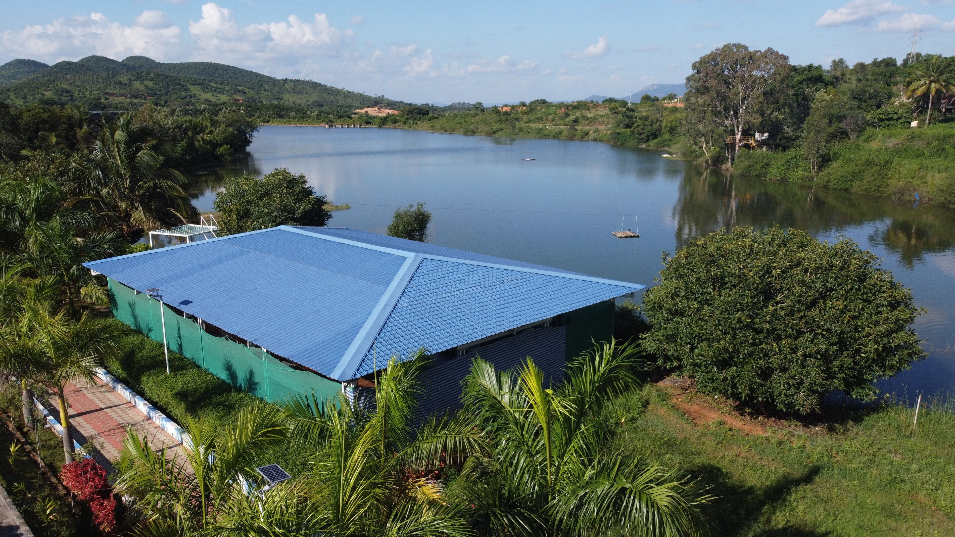 A building with a blue roof near a lake, surrounded by greenery and hills.