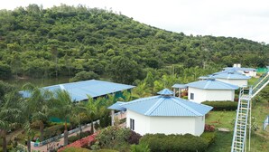 Ein Resort mit mehreren Gebäuden, jedes mit einem blauen Dach, umgeben von üppiger Vegetation und einer Hügelkette im Hintergrund.