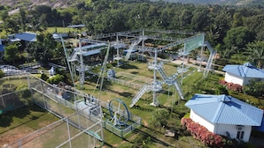 Eine Vogelperspektive eines Parks mit einer großen Metallkonstruktion, möglicherweise eine Spiel- oder Kletterzone, umgeben von Grünflächen und einigen Gebäuden mit blauen Dächern.