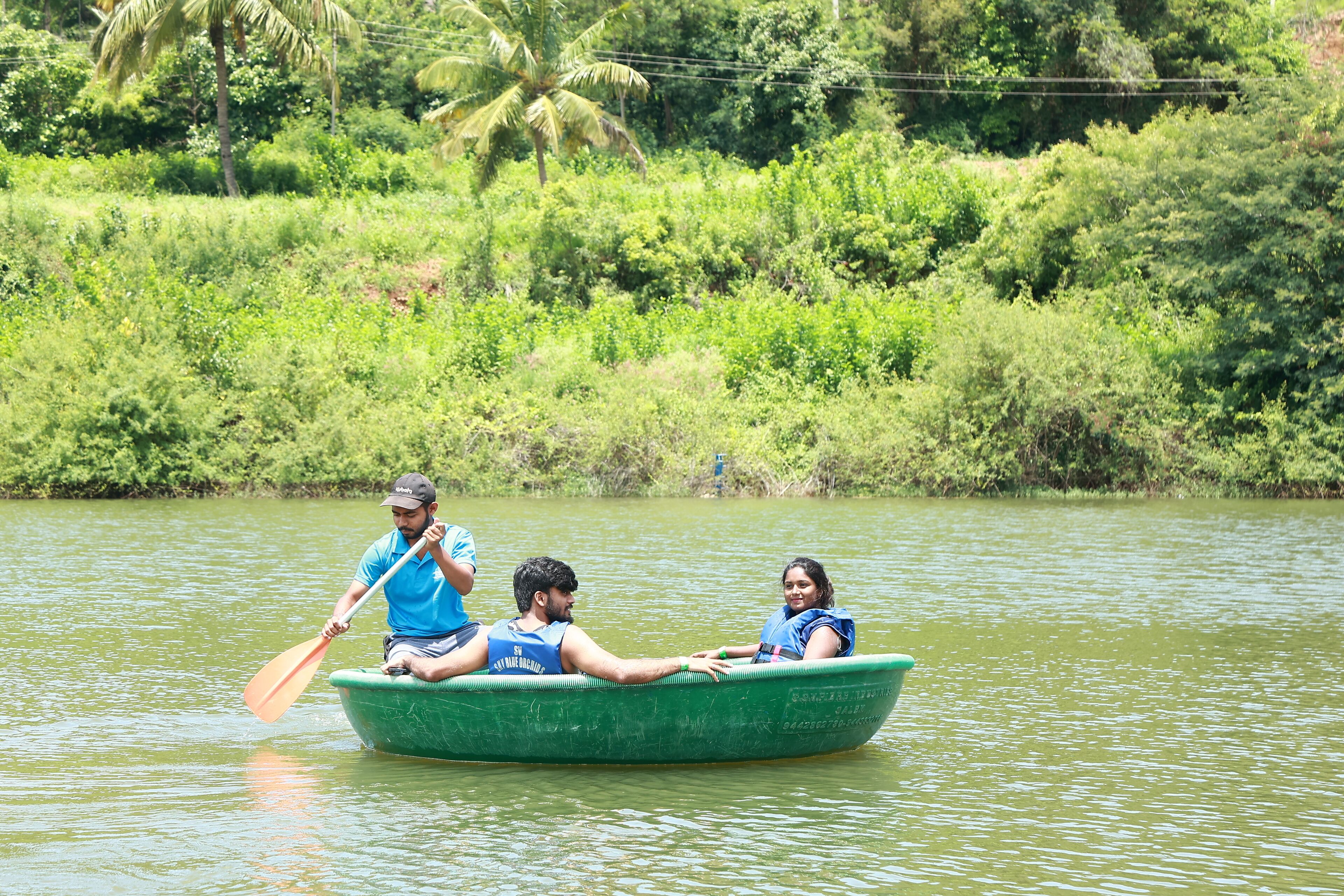 A group of people in a green boat on a calm river surrounded by lush greenery.