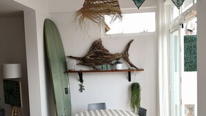 Ein Essbereich mit einem runden Tisch, Stühlen, einem Surfbrett und einer Pendelleuchte.
