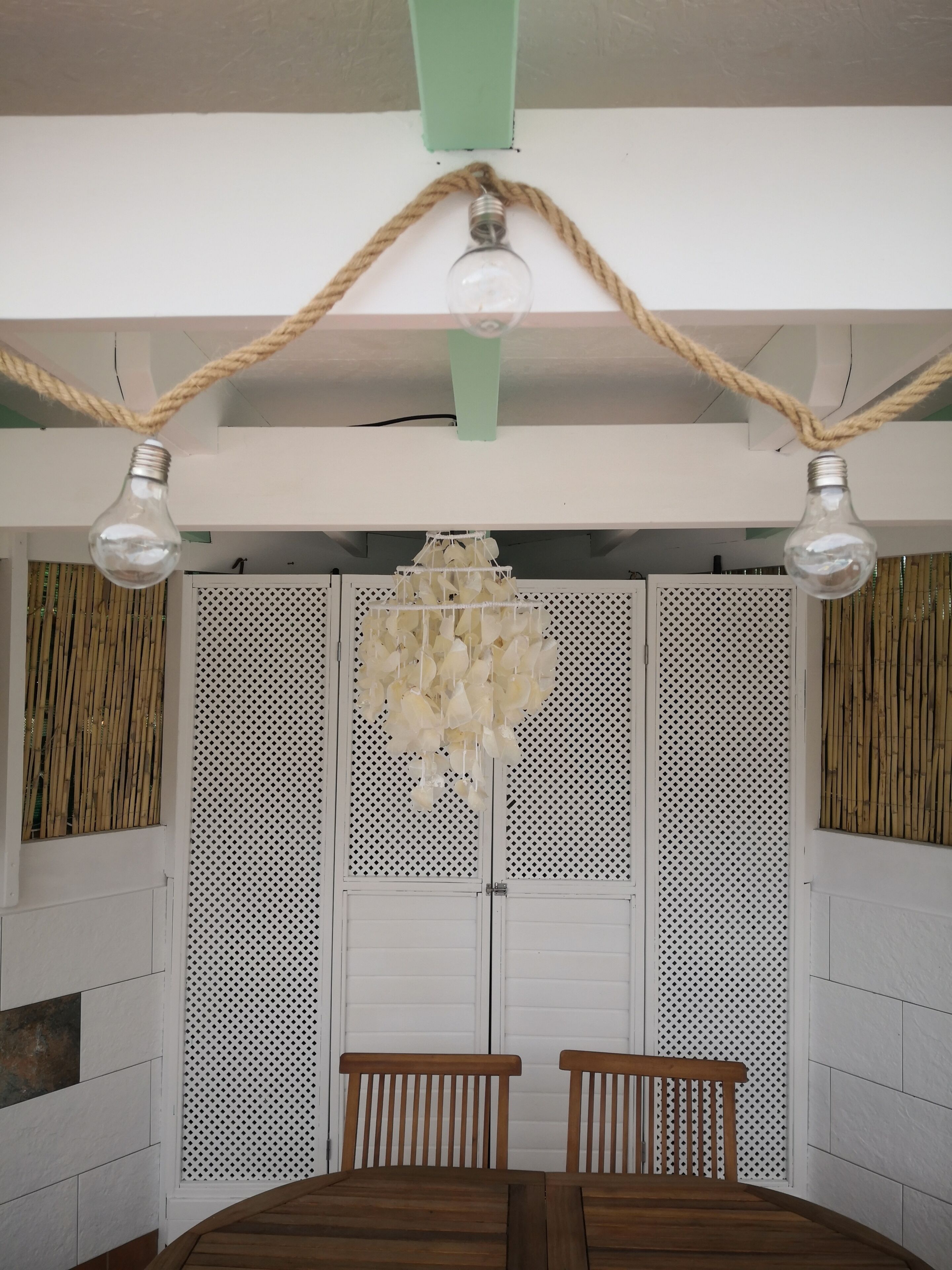 Une pièce comprenant une table à manger en bois, deux chaises, un lustre suspendu et une cloison blanche ornée d’un motif ajouré.