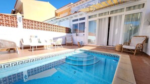 Ein Swimmingpool mit Fliesen umgeben, mit Liegestühlen und einer überdachten Terrasse.