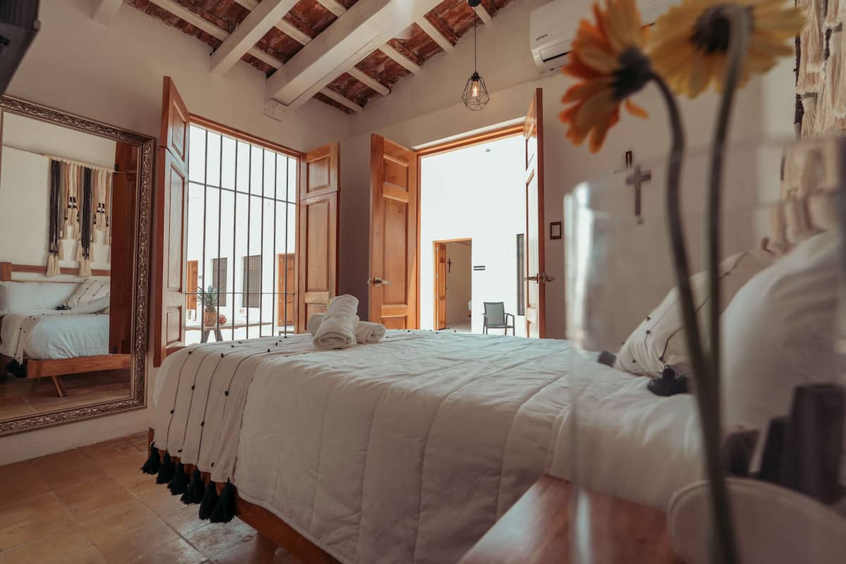 A bedroom with a large bed, wooden beams on the ceiling, a mirror, and a window with a view.