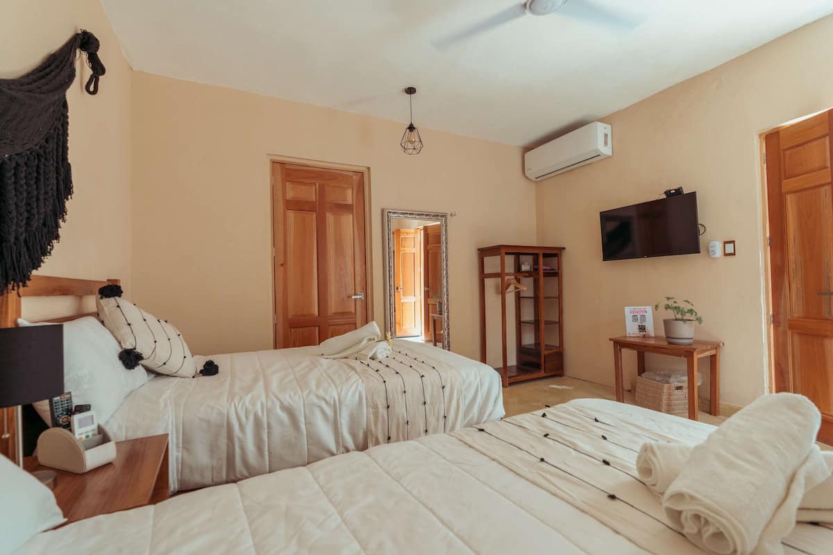 A hotel room with two beds, a TV, an air conditioner, and a wooden wardrobe.