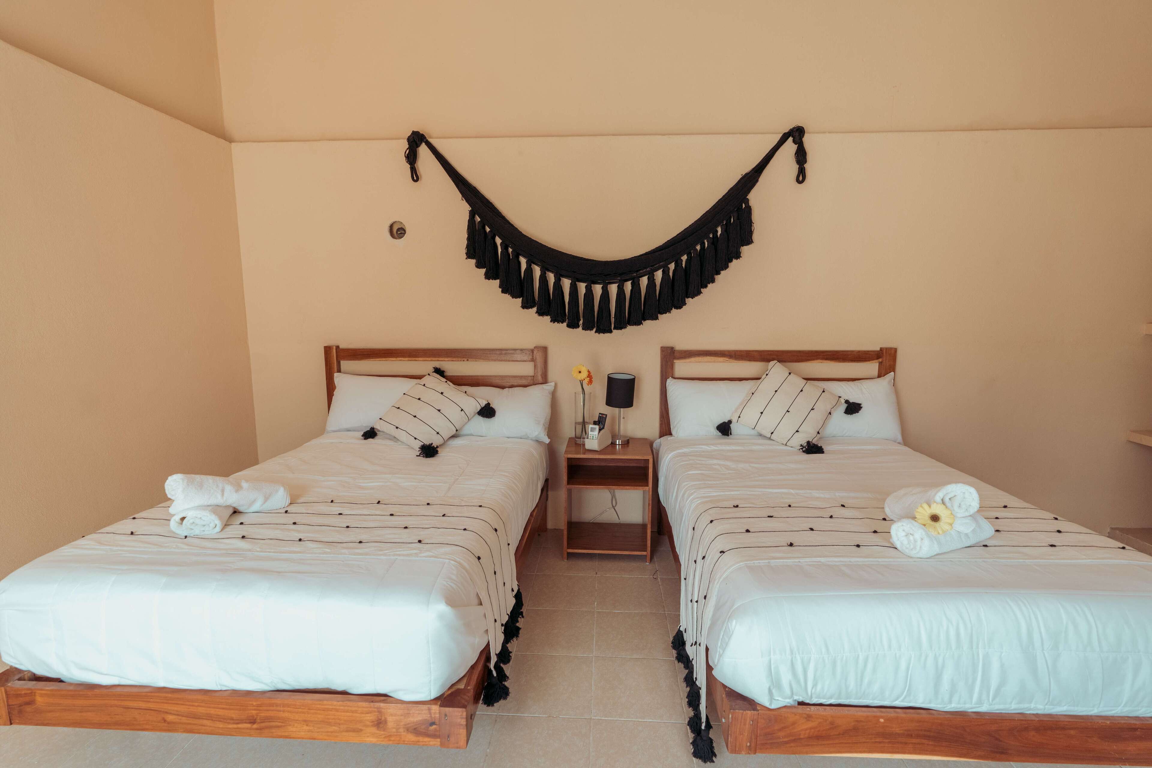 Twee enkele bedden met houten frames, witte beddengoed en zwarte kwastjes aan het plafond.