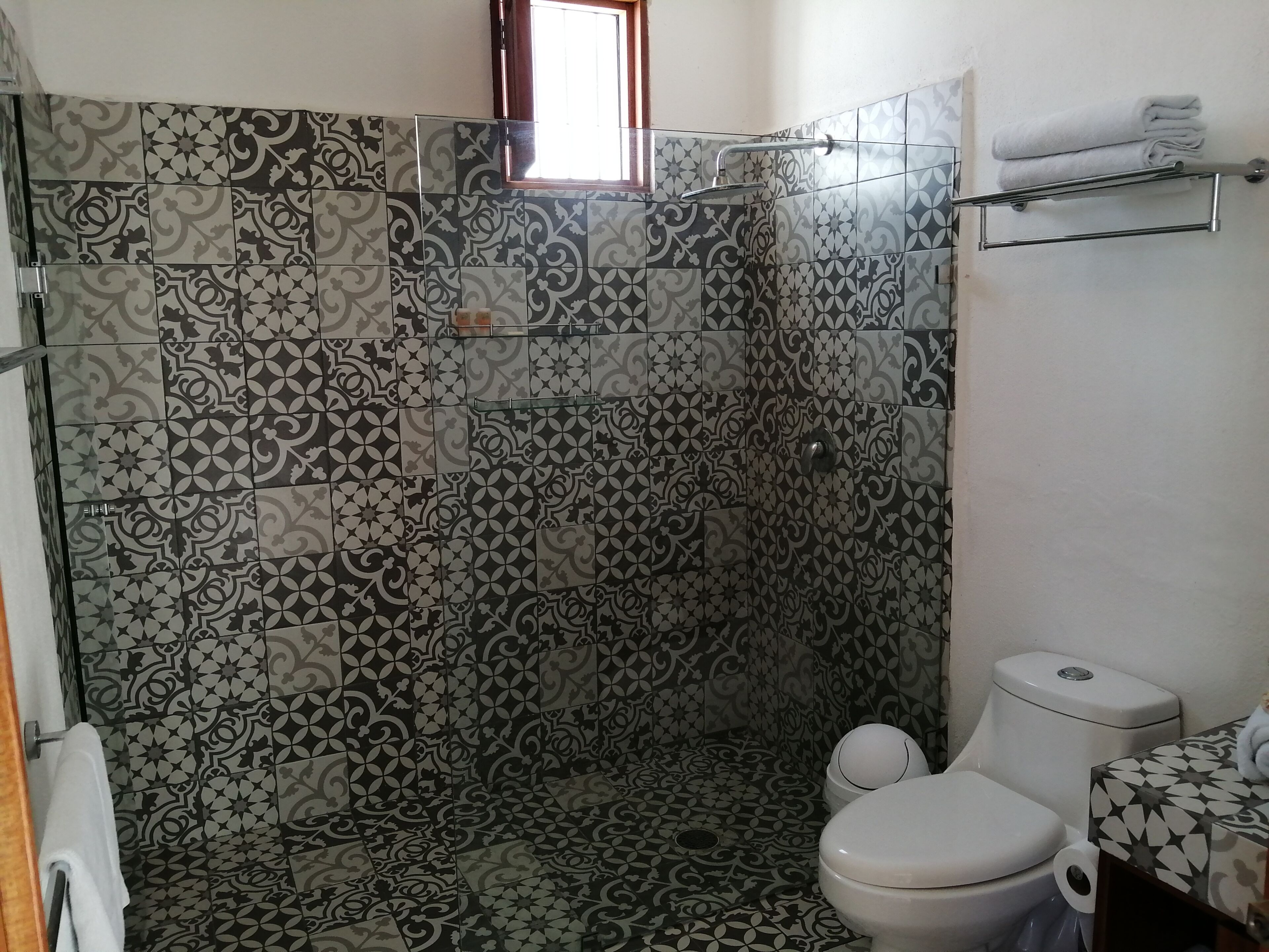 A bathroom with patterned tiles, a shower, a toilet, and a towel rack.
