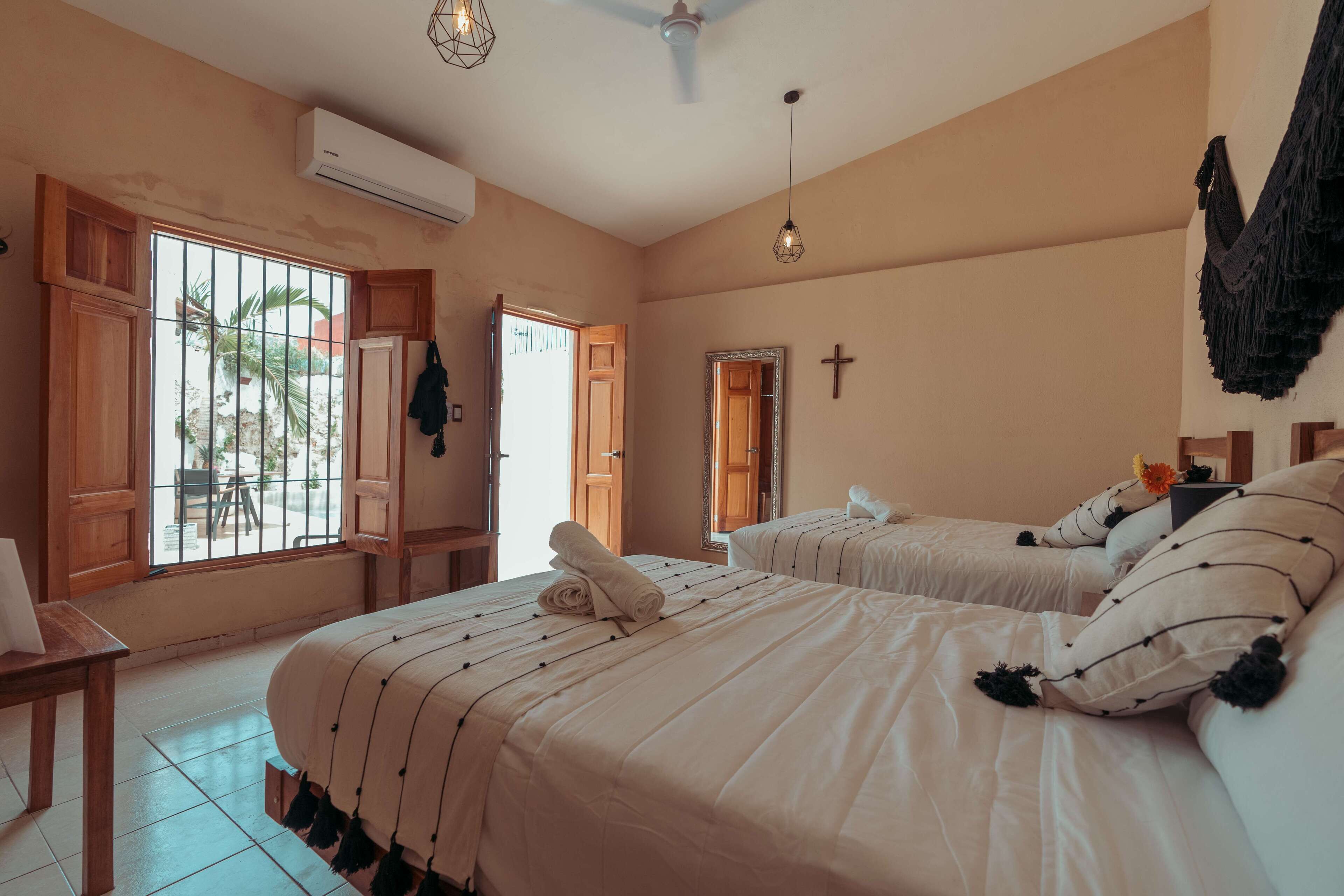 A hotel room with two beds, a desk, and a window with bars.